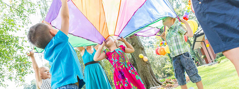 Kinder spielen mit einem bunten Schwungtuch auf einer Sommerwiese